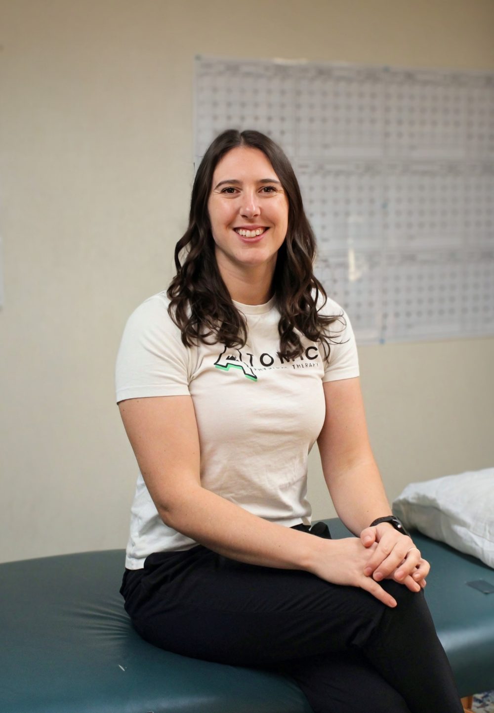 The resident physical therapist from Atomic Physical Therapy, seated on a treatment table inside the club