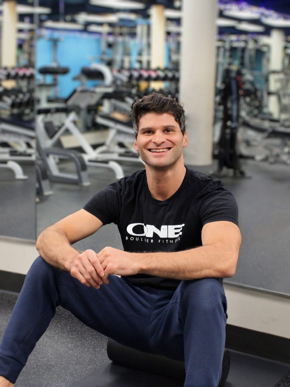 Jesse, personal trainer, sitting on a foam roller on the gym floor