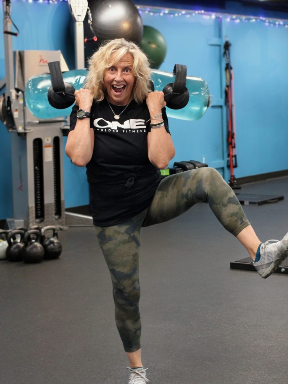 Karie, owner of ONE Boulder Fitness, mid-laugh with dumbbells on the gym floor
