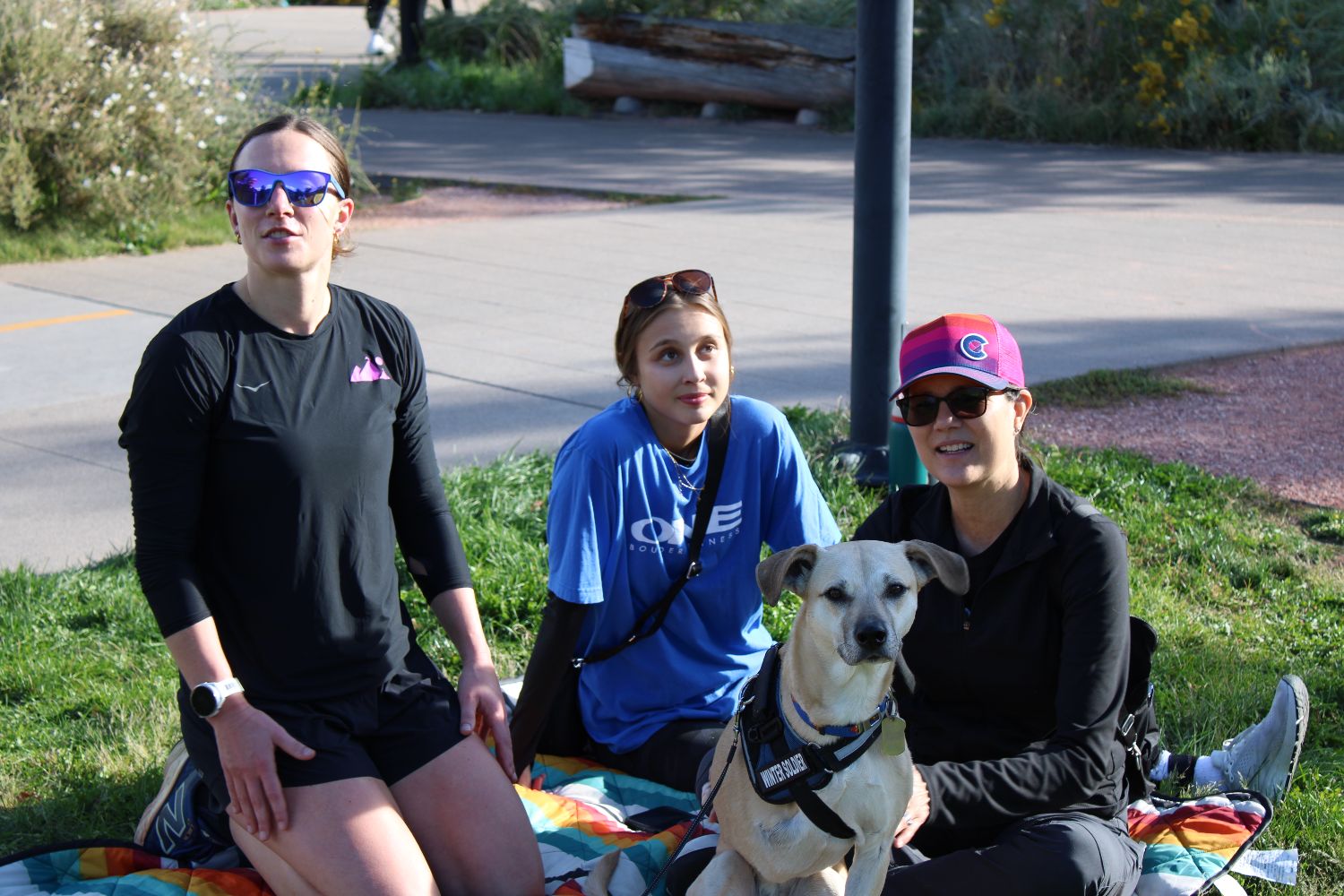 Three members sitting on the grass with a dog after a run