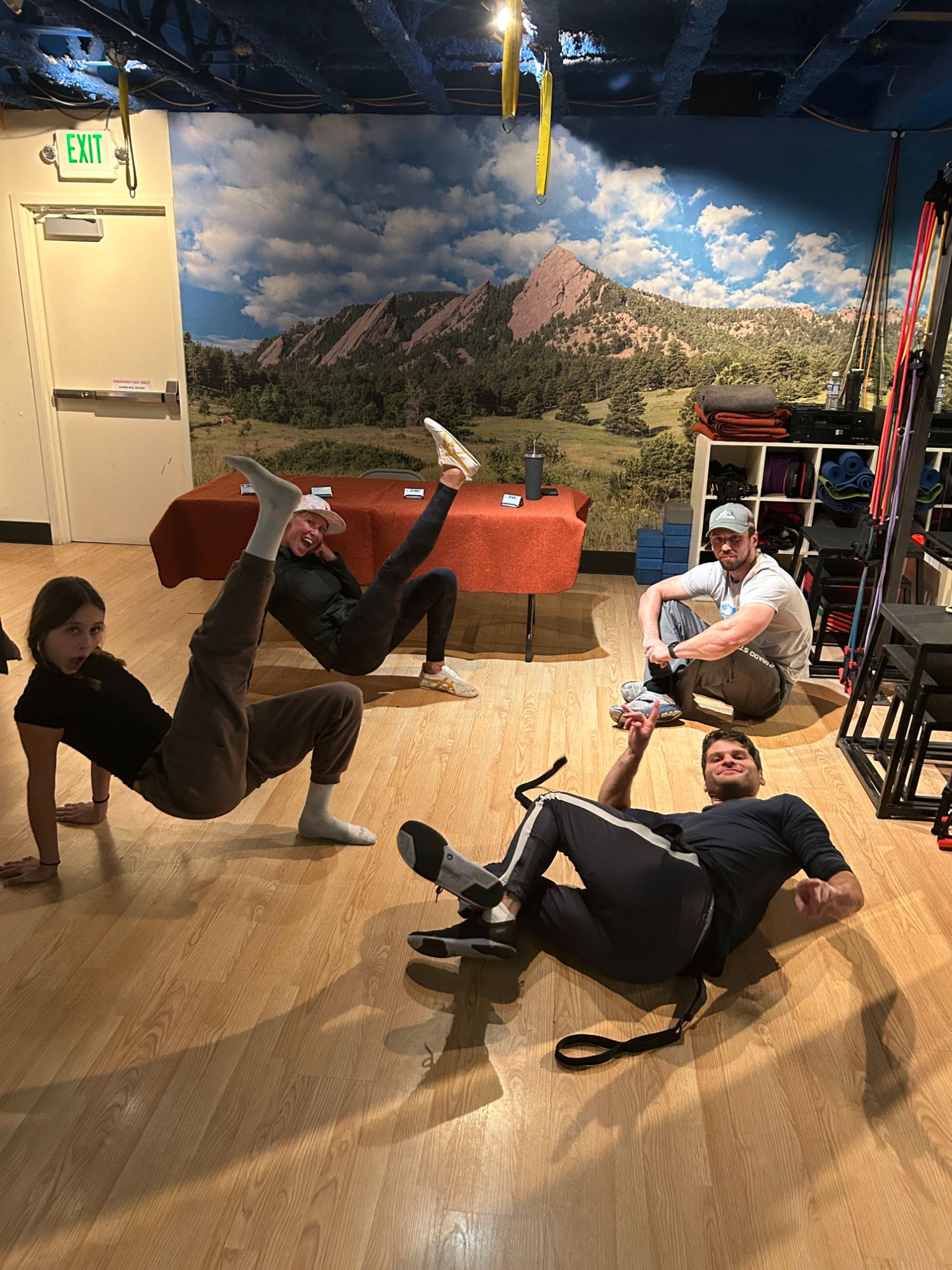 Four members goofing around on the studio floor under the Flatirons mural